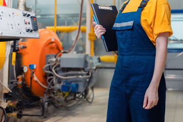 Concept of industrial production and factory. A female worker in uniform with a folder in her hand. In the background, boiler equipment