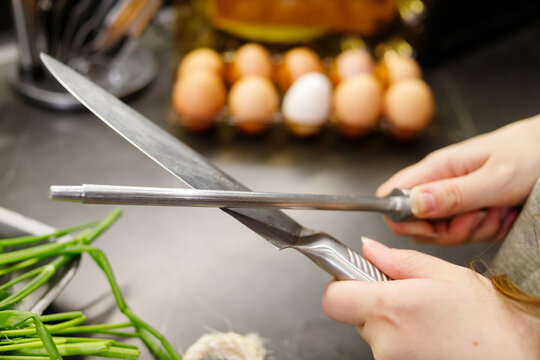 Woman sharpening kitchen knife with grindstone in the kitchen, kitchen knife. Close up view on hands - Powered by Adobe