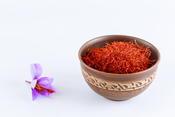 single saffron flower and saffron thread in ceramic bowl on white