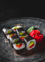 sushi roll with salmon, avocado, rice in plate on black wooden table background