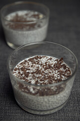 glass of chia pudding with oat milk with chocolate and strawberry shavings on top of blue napkin. healthy food and diet