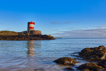 Fototapeta na wymiar Image of Archirondel Bay with the Napoleonic Jersey Tower early on a sunny day, with St Caherines Breakwater in the far back ground.. Jersey, Channel Islands