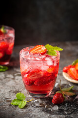 Refreshing summer drink with strawberry slices in glasses on dark background