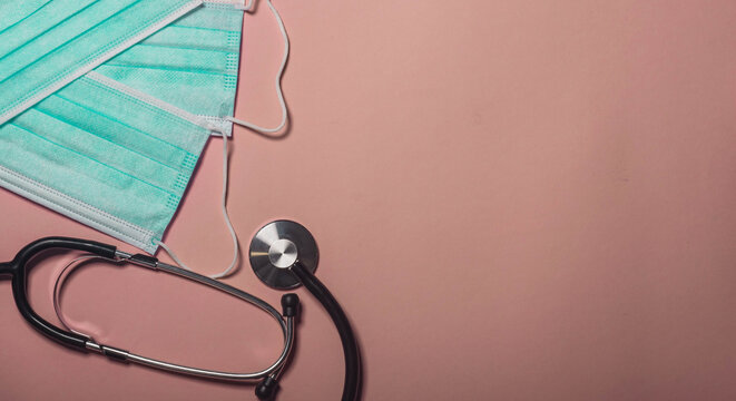 Blue medical surgical mask with rubber ear straps,stethoskop on pink background. Face protective hygienic mask. Protective from Coronavirus Covid-19, flu. Healthcare, medical and new normal concept.