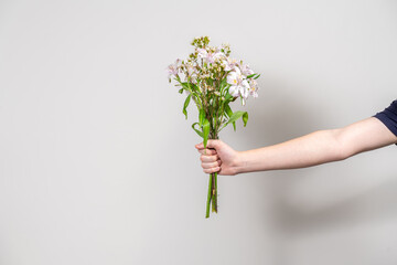 Fototapeta na wymiar hand of a man with a bouquet of white flowers on a gray background
