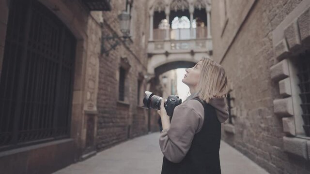 Beautiful Female tourist with dslr photo camera walking through old town narrow streets, Barcelona, Spain. She takes photos. Prores 10 bit color space