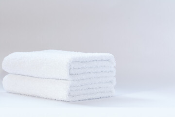 Two white neatly folded terry towels on a light background