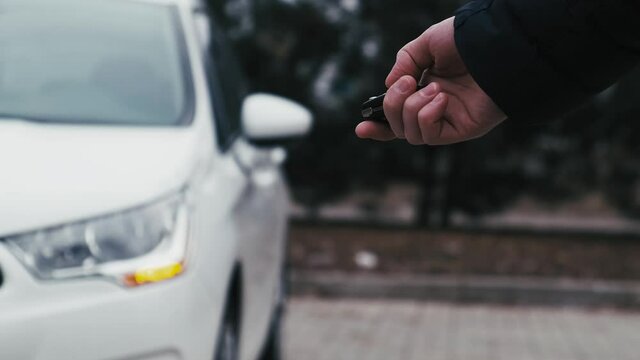 Driver unlocking the car by the car's key remote control with flashing car headlight