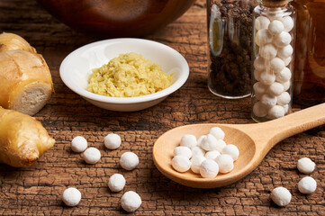 concept of homeopathic pills in a wooden spoon and bottles with herb on wooden table background                    
