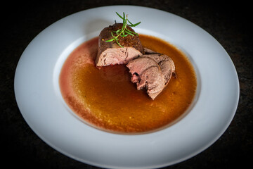 fresh cooking at home and ready to eat, delicious medium roasted game meat from a young chamois with sauce and rosemary on a white plate
