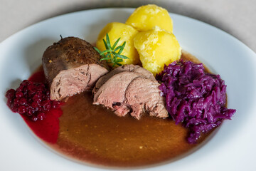 delicious meal from a young chamois buck with potatoes and red cabbage, brown sauce and cranberries on a white plate