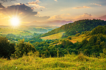 Obraz premium mountainous rural landscape at sunset. beautiful scenery with forests, hills and meadows in evening light. ridge with high peak in the distance. village in the distant valley
