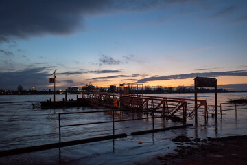 Fototapeta premium Outdoor scenery view of flooded area along riverside of Rhine river in Düsseldorf, Germany during evening time with beautiful sunset and twilight sky.