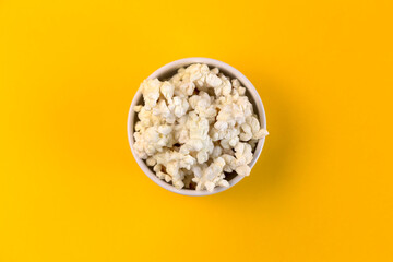 Bowl with popcorn on yellow background.