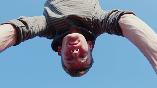 A tense concentrated man doing a handstand on parallel bars. A view from below on a young sportsman training on bars outdoors
