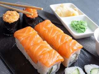 a variety of Japanese rolls and sushi on a textured plate. Side view. bamboo sticks of ginger and sauce nearby.