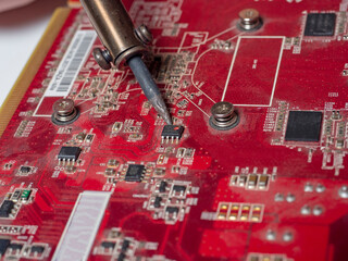 A repairman solders a printed circuit board of an electronic device in red color close-up. Repair...