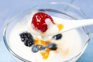 in the foreground a spoonful of low-fat yogurt with red raspberry and forest honey.