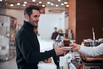 Happy man buying cup of hot drink in cafe