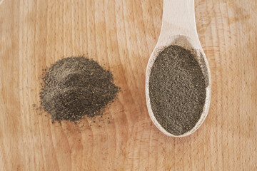 black ground pepper in a wooden spoon on a wooden background. A pile of ground pepper.