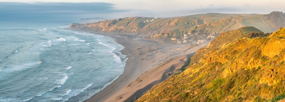 An idyllic coastline view with the waves from the ocean smashing the sand in the coast. An amazing place to live in connection with nature in a wild place inside the beach sand dunes below the cliffs