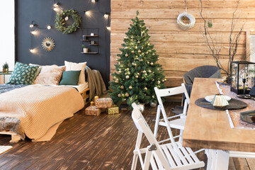 On the eve of the holiday, the interior of the country house is decorated with a New Year tree. large spacious light room decorated with wood with simple wood furniture