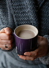 The girl in a cozy knitted sweater drinking coffee from a purple mug