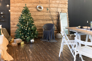 On the eve of the holiday, the interior of the country house is decorated with a New Year tree. large spacious light room decorated with wood with simple wood furniture