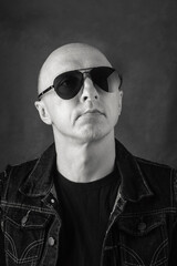 Obraz premium Unshaven, bald middle-aged man in a black T-shirt, denim vest and dark glasses. Black and white portrait. Photo taken in studio