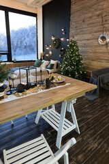 On the eve of the holiday, the interior of the country house is decorated with a New Year tree. large spacious light room decorated with wood with simple wood furniture