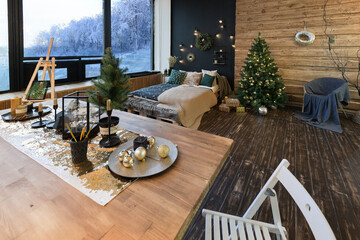 On the eve of the holiday, the interior of the country house is decorated with a New Year tree. large spacious light room decorated with wood with simple wood furniture