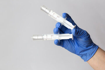 Obraz premium A human hand in a blue protective glove holds twoo syringes between his fingers. White background.