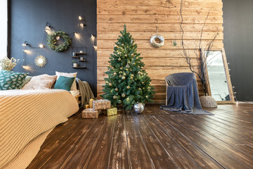 On the eve of the holiday, the interior of the country house is decorated with a New Year tree. large spacious light room decorated with wood with simple wood furniture