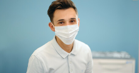 Portrait of a young smiling dentist turkish ethnicity wearing facial mask. Portrait of a male medic on a blue background. 4k video screenshot, please use in small size
