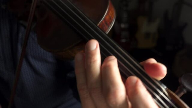 A violinist playing the violin in a studio. Using a bow to play an old violin with focus on the left hand fingers on the fingerboard.