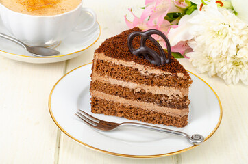 Piece of chocolate cake, cappuccino, flowers on table