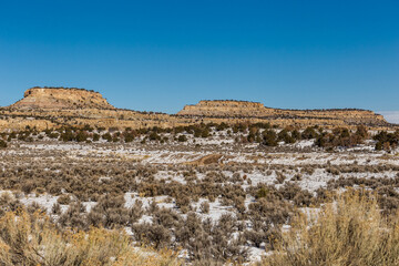 Wide open desert vista covered in snow with rocky mesa plateau mountains on clear day in rural New Mexico