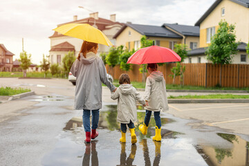 Happy family: mother, daughter, son stand under umbrellas. Mom and children go home in puddles in the rain on the street