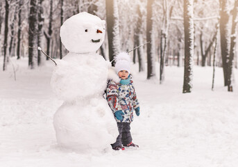 Little girl and a big winter snowman in the park
