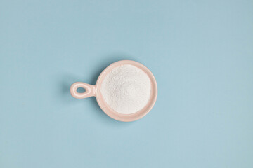 Collagen powder or protein in pink bowl on a blue background with copy space. Top view. Cosmetic skin care concept.