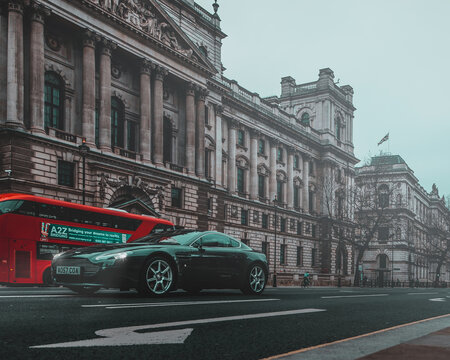 London UK January 2021 Black Aston Martin DB9 on the streets of London, red double decker bus passing behind it. Cold foggy winter day