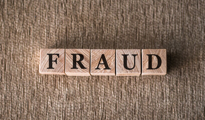 FRAUD word written on wooden blocks on a brown background.