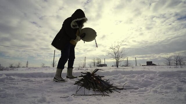 The witchdoctor conjures the spirits of fire with a stone on a tambourine near the fire in the snow
