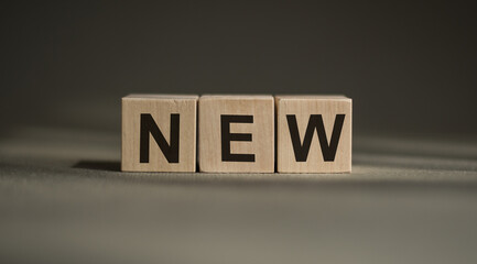 A wooden blocks with the word NEW written on it on a gray background.