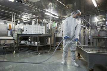 Wide angle full length portrait of female worker washing equipment at clean food production...
