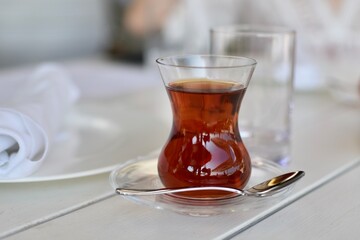 Turkish tea in a traditional glass and a spoon on white table