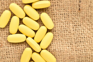 Several oval yellow pills on a jute cloth, close-up, top view.