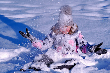 Obraz premium The girl plays with snow. Child rejoices in winter. Happy childhood.