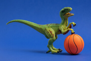 Fototapeta premium Green dinosaur toy with basketball ball. Basketball minimal card blue background.