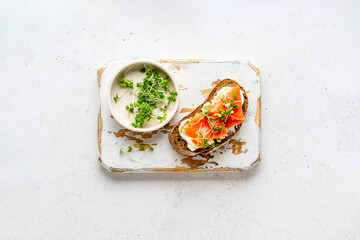 Toasted bread with ricotta (cream cheese), smoked salmon and micro greens served on wooden rustic board. Health care, super food concept. White Stone background. Top view.